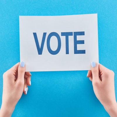 cropped view of woman holding white card with vote lettering on blue background